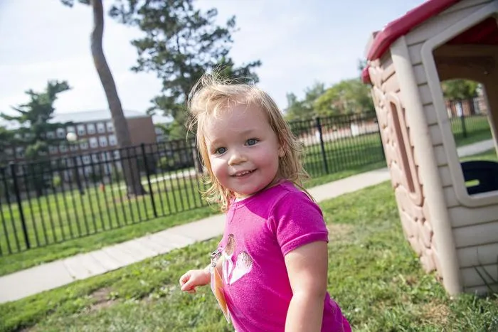 Toddler standing outside by a play structure on a lawn