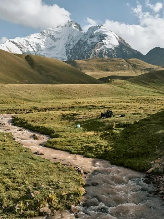 A stream with mountain glaciers and snow that supply it in the background